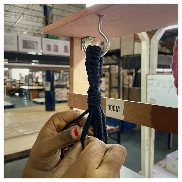 A person holding a black cotton macramé plant hanger with a metal hook, marked 10cm.