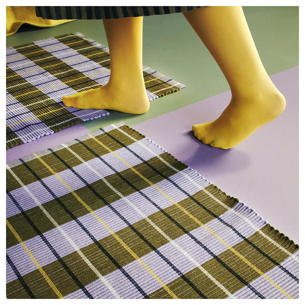 Feet on yellow socks step on yellow, green, and blue chequered rug.