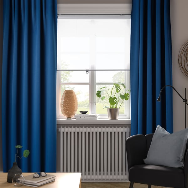 Dark blue MAJGULL curtains frame large window with soft fabric. Plant, decor, black chair with blue pillow, and modern lamp below.