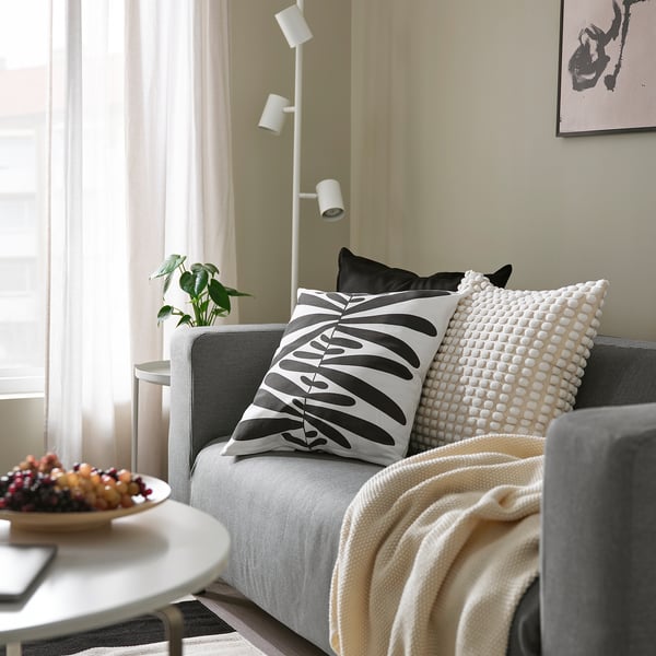 Modern living room with grey and cream pillows, beige blanket on sofa, and fruit bowl on wooden table.