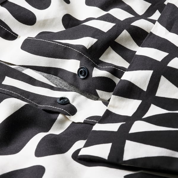 Close-up of duvet cover with black leaf prints, showing plastic press-stud closure at bottom.