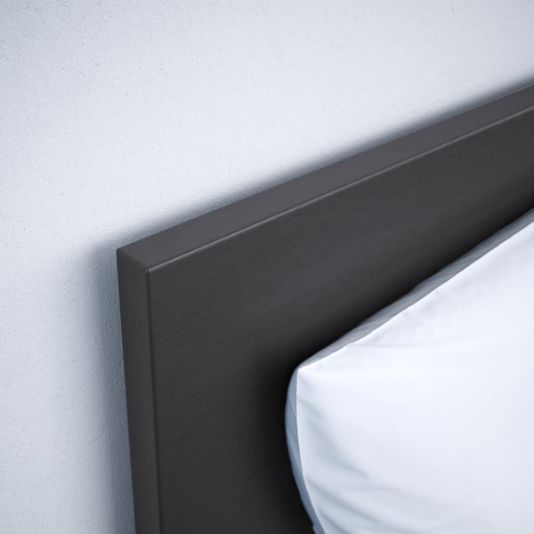 Black wooden headboard corner against a light wall, showing smooth finish and sleek design.