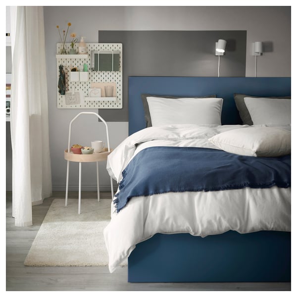Modern bedroom with blue MALM bed, white linens, small round tray table, decorative wall shelves, and rug.