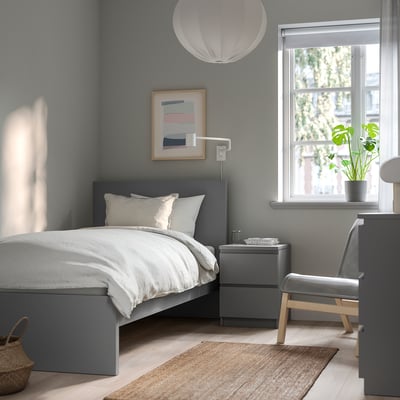 Minimalist grey MALM bed, large, with white linens, bedside table, and art. A large window lets in natural light.