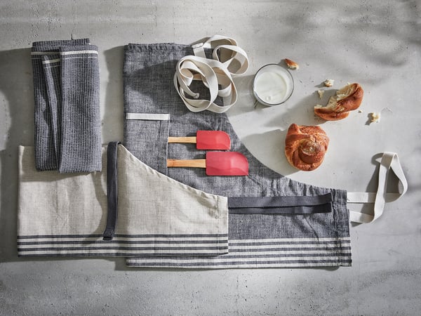 Six striped MARIATHERES grey towels in cotton/linen blend, with two red spatulas and two rolls, displayed on a light grey wall.