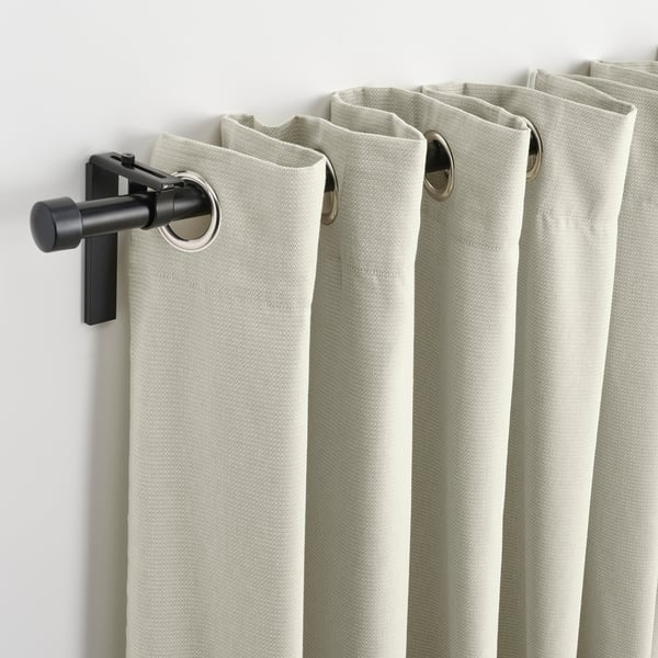 Beige curtains with black eyelet headers hang on wall mount, offering light control and privacy.