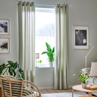 Bright room with green curtains, wicker chair, and plant near window.