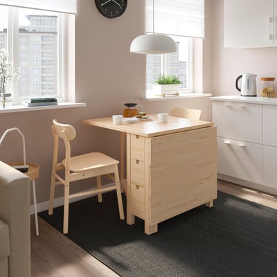Small light wood NORDEN dining set with table, two chairs, and rug in a cosy kitchen space.