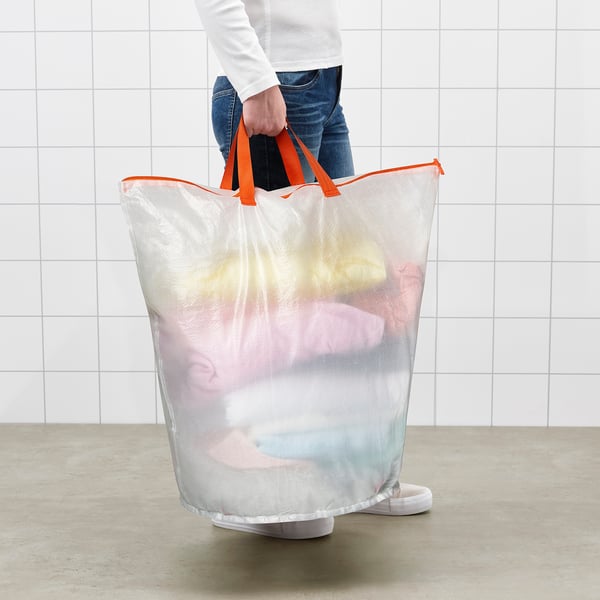 Person holding a mesh laundry bag with bright orange handles filled with clothes.