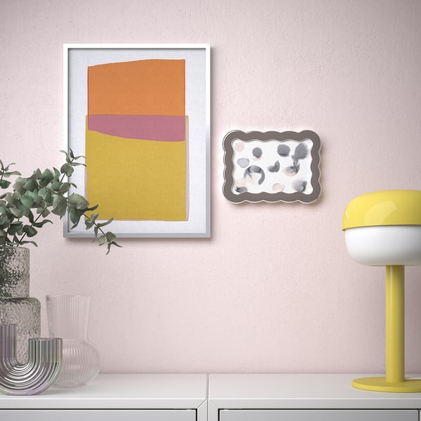 Wall art display with colourful geometric print and decorative tray on pastel pink wall.