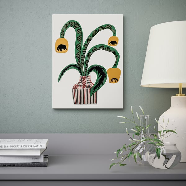 Canvas art with green plants on blue wall, books, plant, & lamp below.