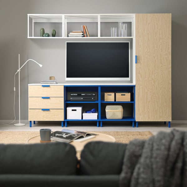 Modern living room with a blue and wood PLATSA storage unit, holding a tv. The unit is large, taller than a grey armchair, and wider than a tall lamp.