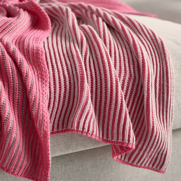Pink striped blanket with soft, textured knit pattern draped over bed.