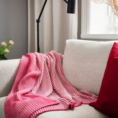 Red & white striped throw on grey couch with lamp & flowers.