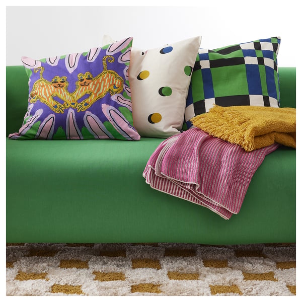 Bright green sofa with multicoloured pillows and folded pink and yellow blankets on it.