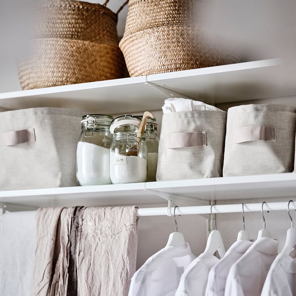 Closet shelf with wicker baskets, fabric storage bins, and clothes hangers, featuring PURRPINGLA white linen fabric basket.