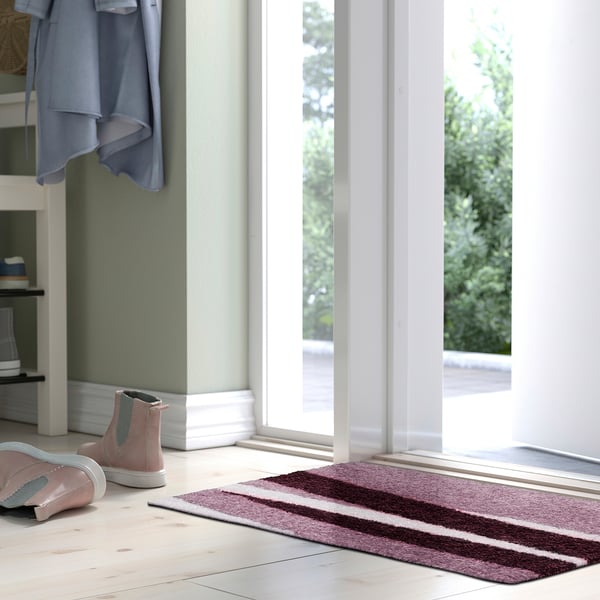 Bright doorstep with RASTFICKA mat, pink boots, and hanging jacket, emphasising mats size and colour.