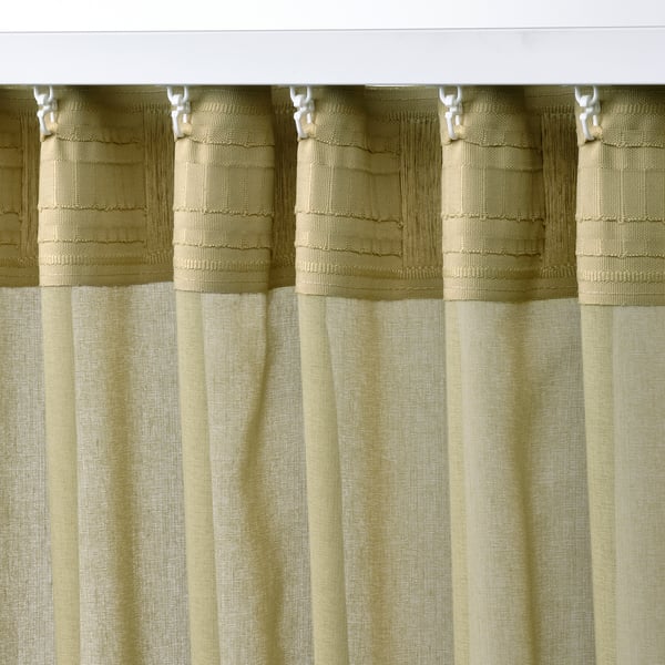 Light olive green sheer curtains hang, filtering light, with rod pocket and tabs for easy hanging.