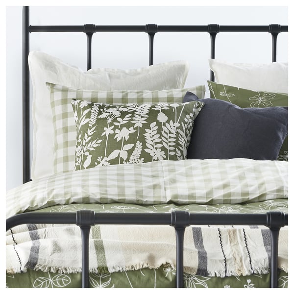 Bed with green-white chequered and floral pillows. Black metal bed frame.