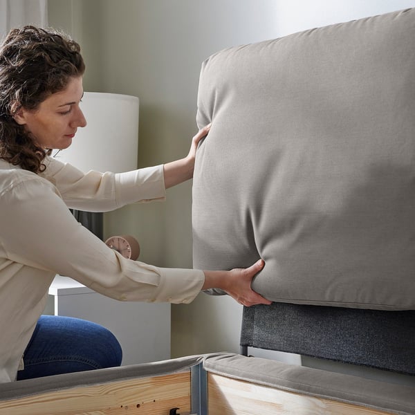 Person placing washable bed cover on stylish, sloped-bed with wooden legs.