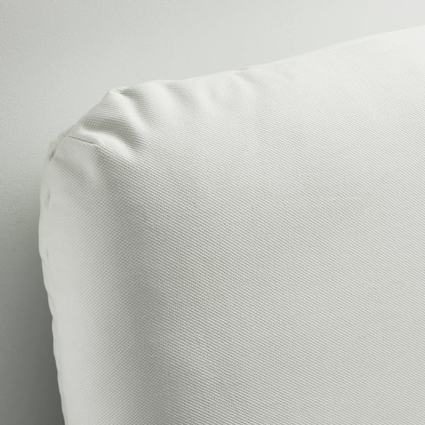 Close-up of a soft, white, upholstered beds headboard and pillow. Fabric appears smooth and clean.
