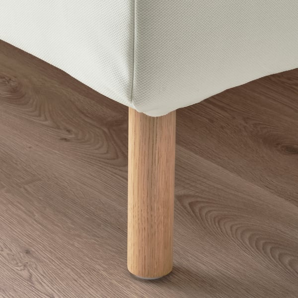 Modern bed with plush headrest, wooden legs, on wooden floor.