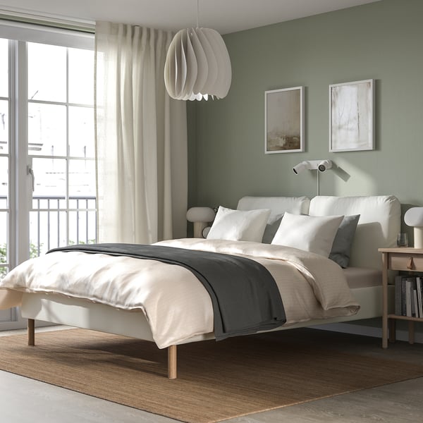 Modern bedroom with SAGESUND bed, high headboard, storage, large window, art, bedside table, warm rug.