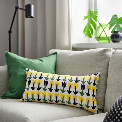 Colourful tulip-patterned cushion on light sofa, with green pillow, throw pillow, plant, and lamp.