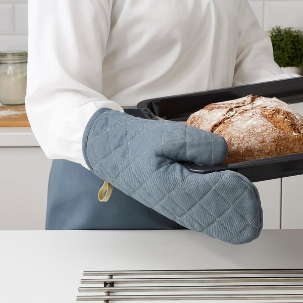 Person wearing a grey oven mitt, holding a tray with a freshly baked loaf of bread in a modern kitchen.