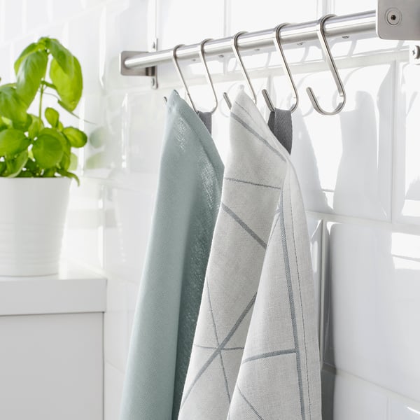 Kitchen towels hang on white rail hooks, next to green plant.
