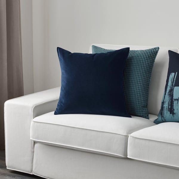 A SANELA navy blue velvet cushion on a white sofa. Its square-shaped, adding a rich, soft touch, and fits well among other cushions.