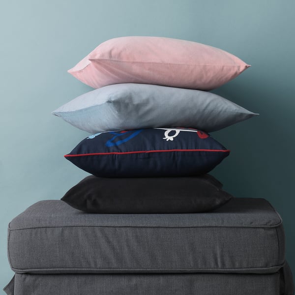 Stack of four decorative throw pillows in pink, grey, navy blue, and black on a dark grey sofa. Each pillow has a zip for easy cover removal.