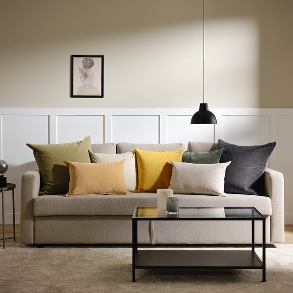 Modern living room with grey sofa, colourful cushions, black coffee table, hanging light, and wall artwork.