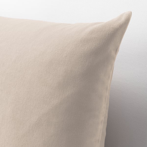 Beige velvet cushion, soft and textured, against striped grey wall, illustrating its luxurious fabric quality.