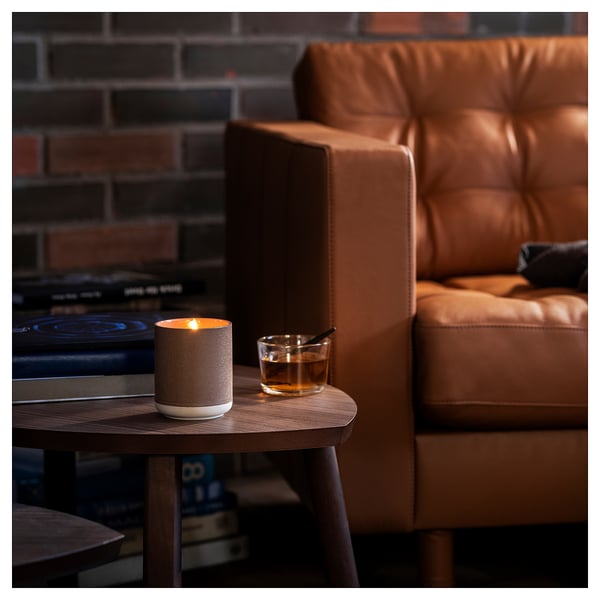 Brown leather chair beside wooden table with lit beige candle and whiskey glass. Cosy indoor setting.