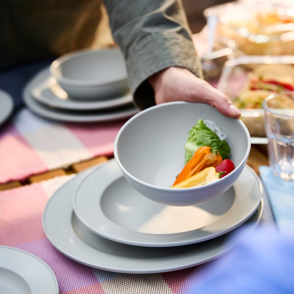 Sgrabba grey bowl filled with veggies on stacked plates, held by a hand.