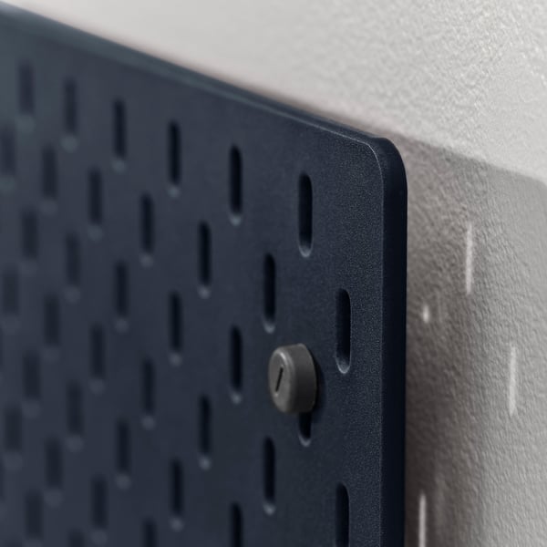 Dark grey metal pegboard mounted on a white wall. Close-up shows sturdy design and a mounted accessory.