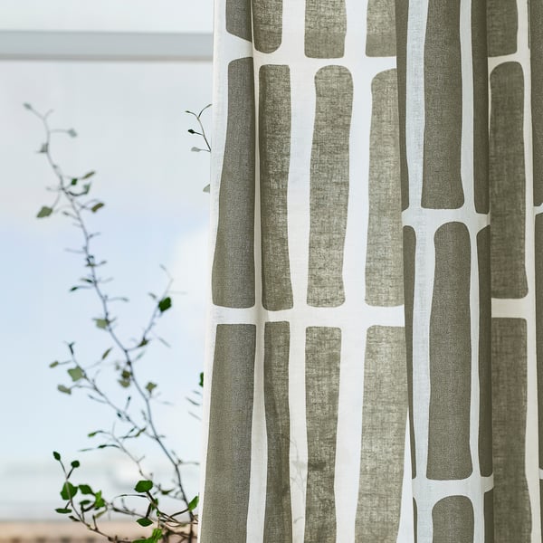 Patterned curtains with vertical lines hang by a window, filtering light and offering daytime privacy. A plant is visible in the background.