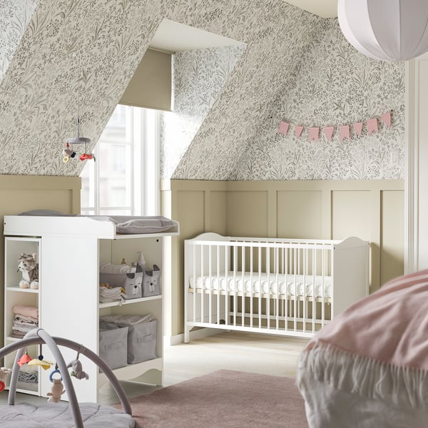 Cosy nursery with SMÅGÖRA white crib, changing table, and shelves. Floral wallpaper, natural light, and soft pink accents.