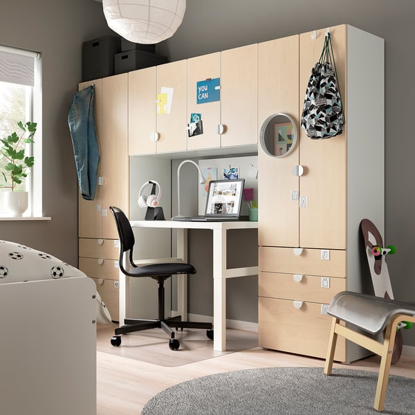 Modern kids room with light wooden desk and cabinet, black chair, laptop, headphones, and backpack; grey rug and toy.