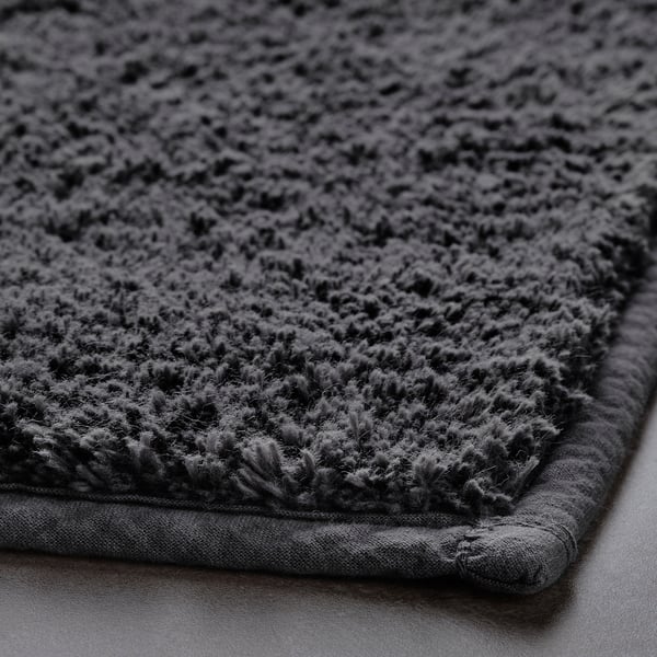Thick, plush bath mat with soft cotton surface and latex backing for stability. Simple, dark-colored design.