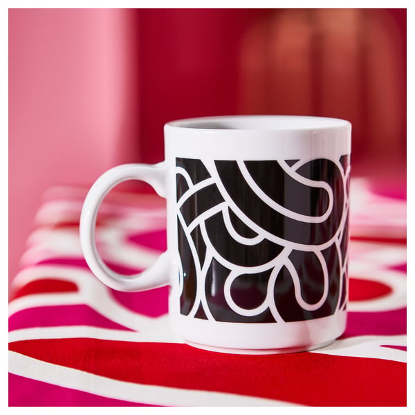 White SÖTRÖNN mug with black abstract patterns on red/white striped cloth. Simple, modern design, slightly larger than average.