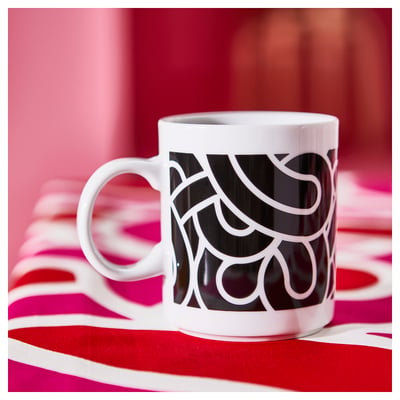 White SÖTRÖNN mug with black abstract patterns on red/white striped cloth. Simple, modern design, slightly larger than average.