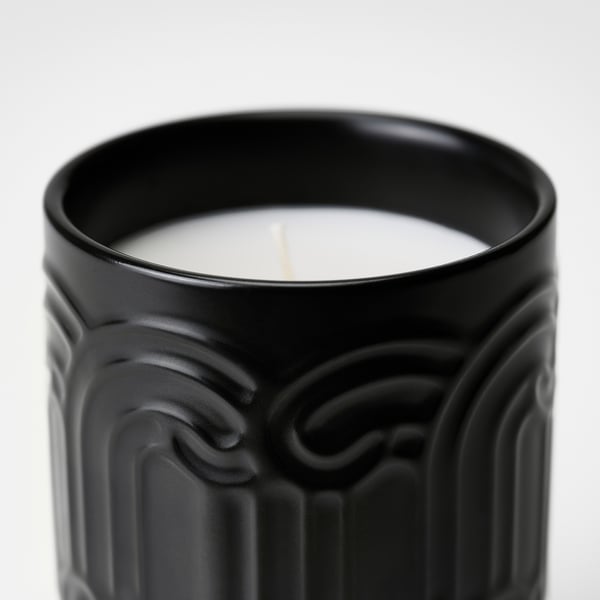 Black stoneware candle with intricate design, featuring a lit wick, emitting a fresh, subtle glow.