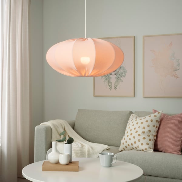 Cosy living room with peach SOLHETTA lamp, grey sofa, side table, mug, vases, blanket, floral art.