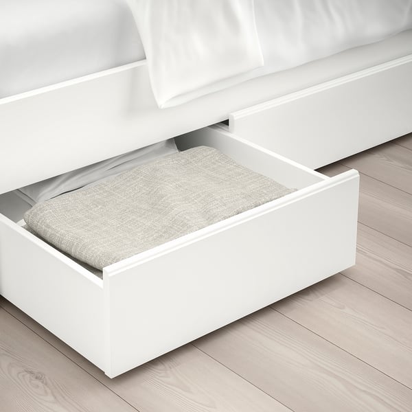 Buttery white bed with large under-bed storage drawer open, revealing folded linens on light wood floor.