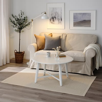 Living room with beige rug, sofa, coffee table, lamp, plant, & artwork.