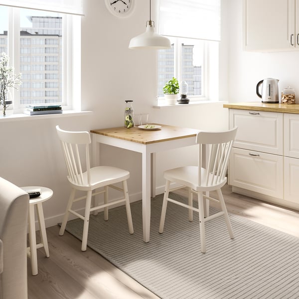 Small white dining set with a natural-toned rug, matching cabinet and chairs, and kitchen counter.