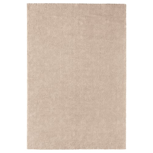 A beige ikea STOENSE area rug with a soft, thick pile, providing comfort and warmth. It has a light sheen, rectangular shape, and a smooth edge.