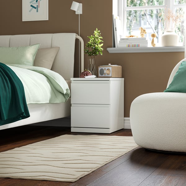 Modern bedroom with STORKLINTA bedside table, plant, clock, chair, and large window.